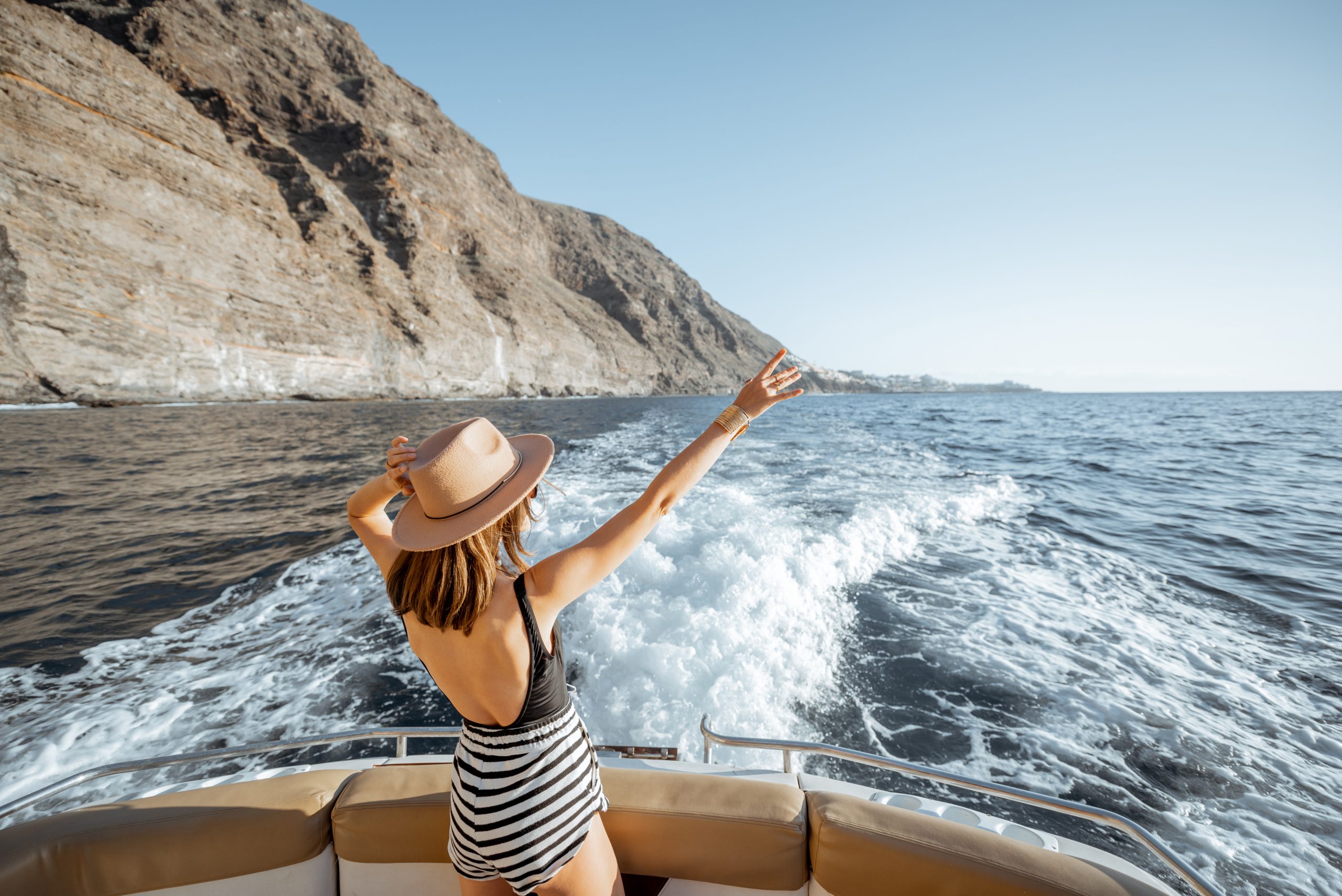 Relaxed woman sailing on the yacht near the rocky coast